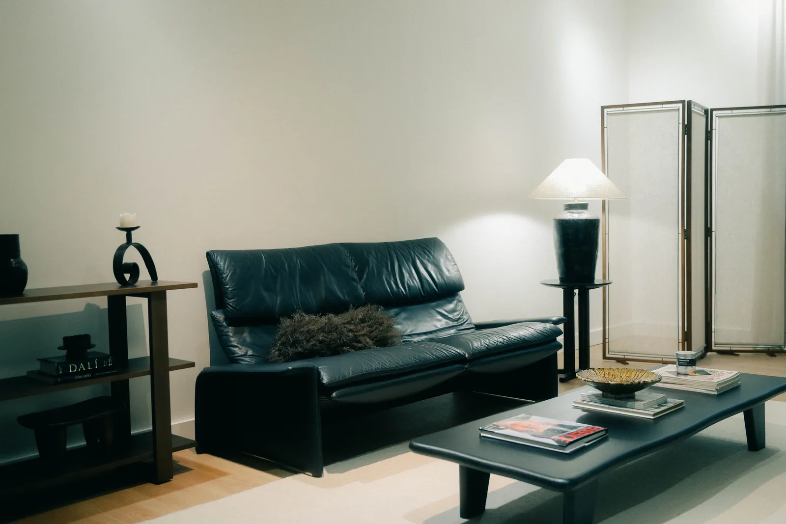 Canapé en cuir noir, table basse et lampe d'appoint dans un salon lumineux.