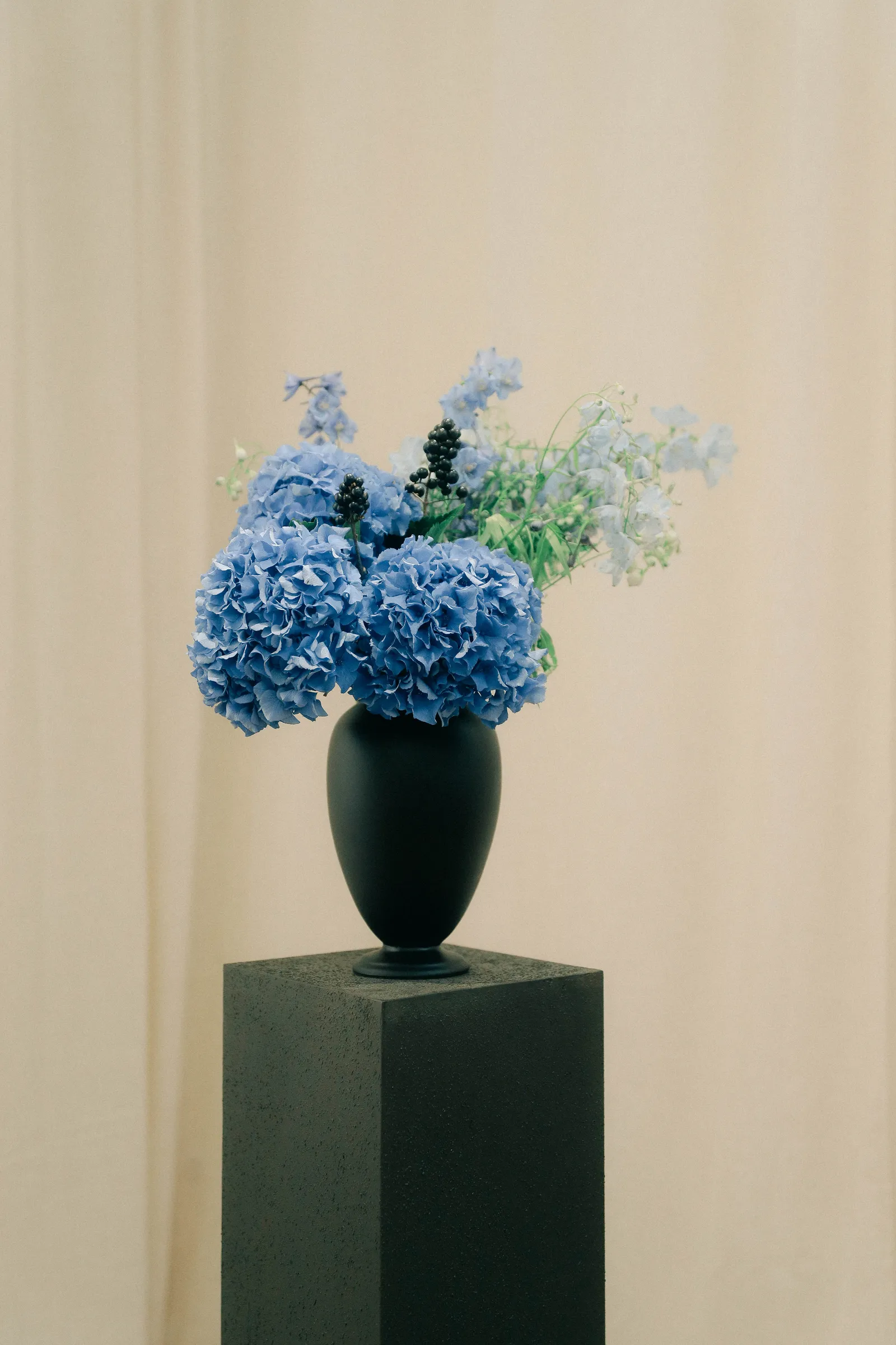 Bouquet d'hortensias bleus dans un vase noir, posé sur un socle sombre.