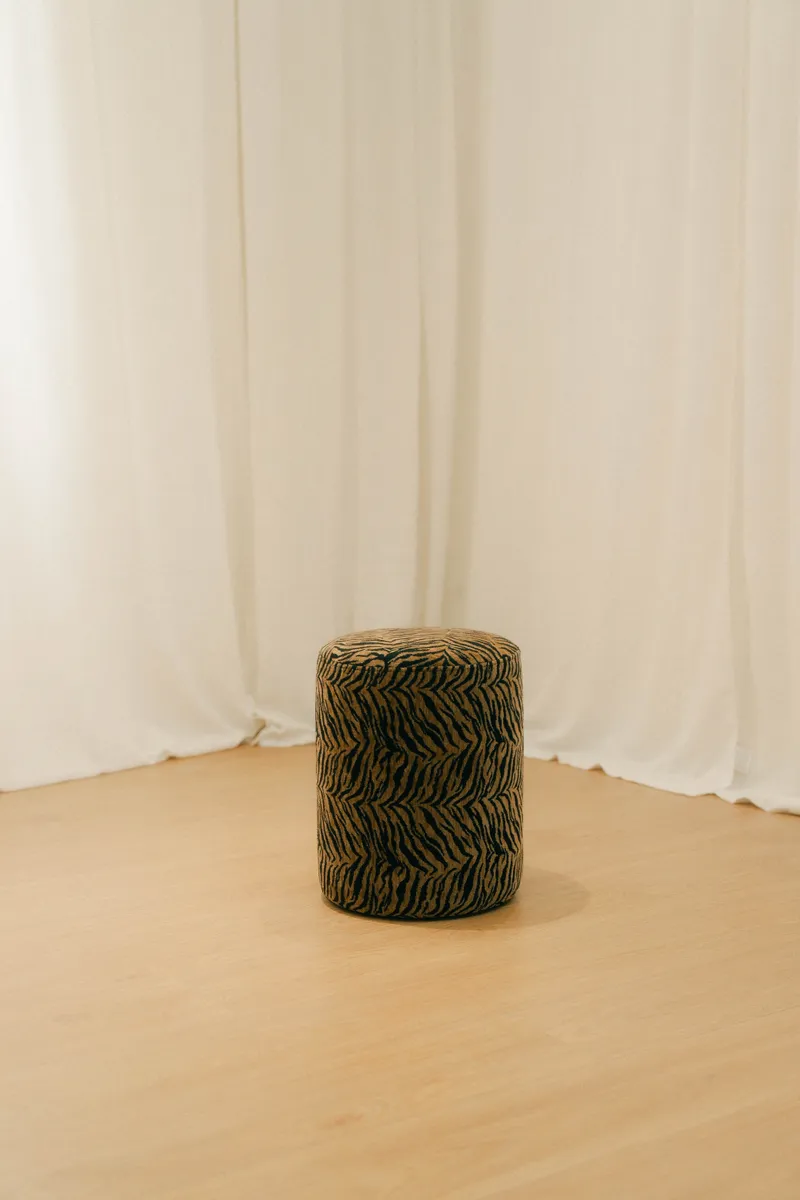 Tabouret rond à motif léopard, devant un rideau de lin.